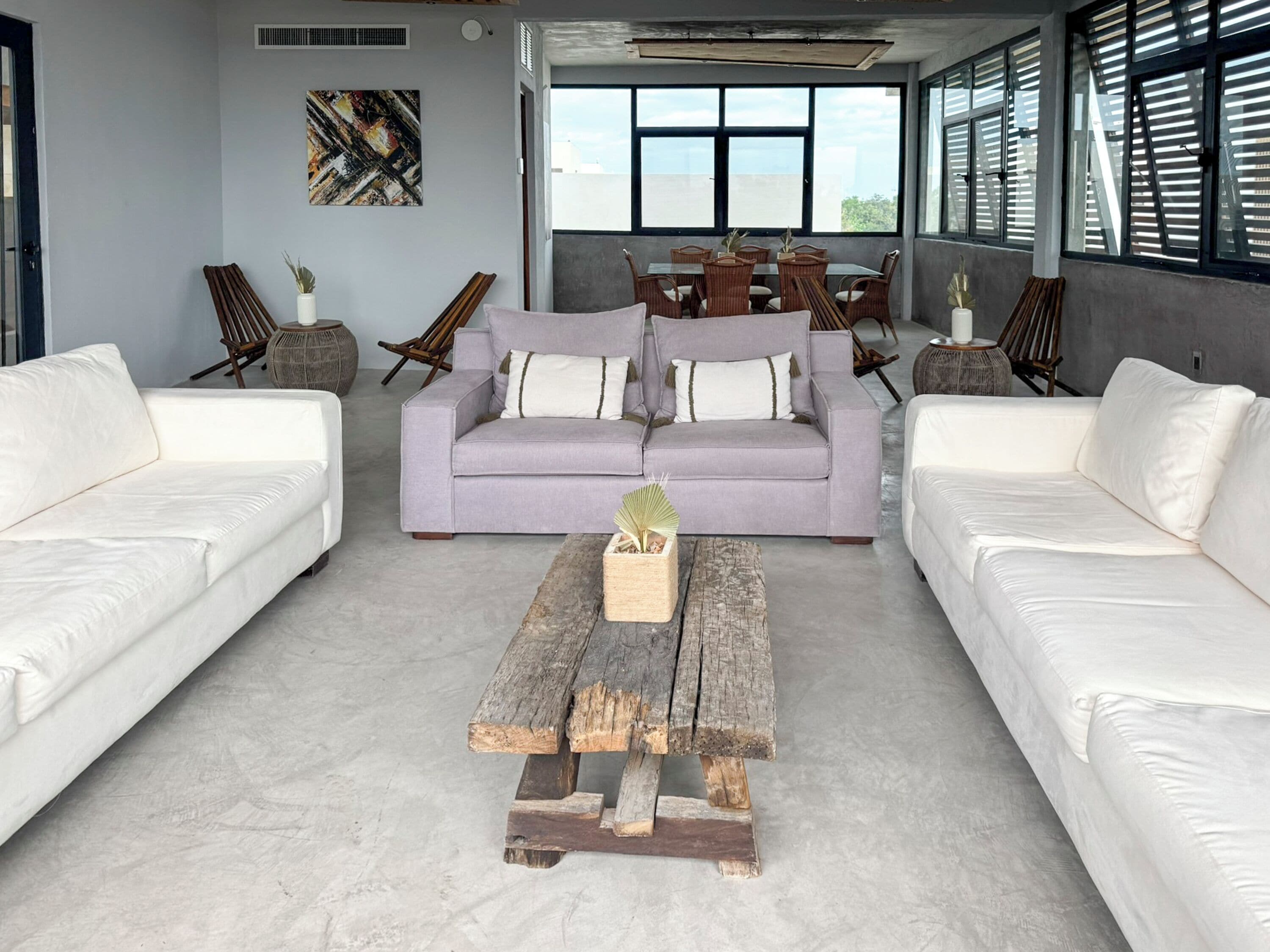 A modern living room with two white sofas, a wooden coffee table, and a dining area with wicker furniture.