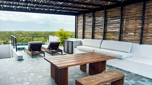 A rooftop terrace with a wooden table and benches, a white sofa, and a view of the cityscape. - Zel-va Tulum (Tulum)