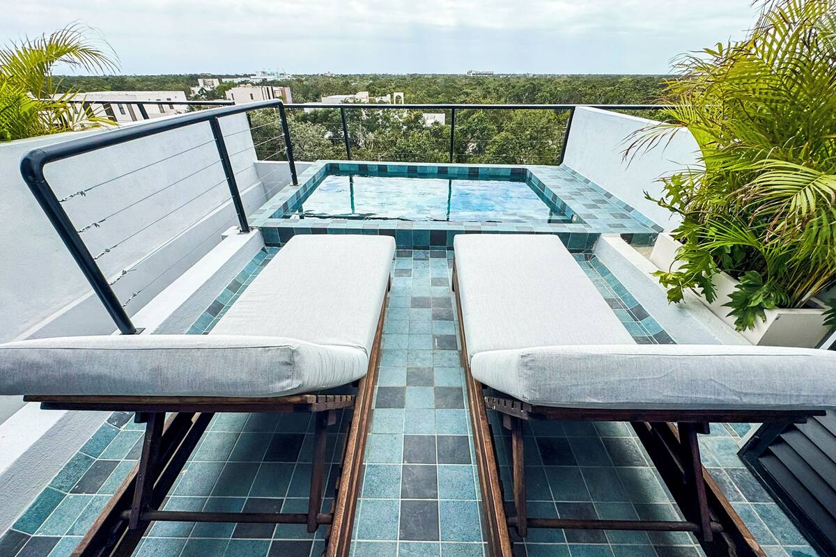 A rooftop pool area with two lounge chairs and a hot tub.