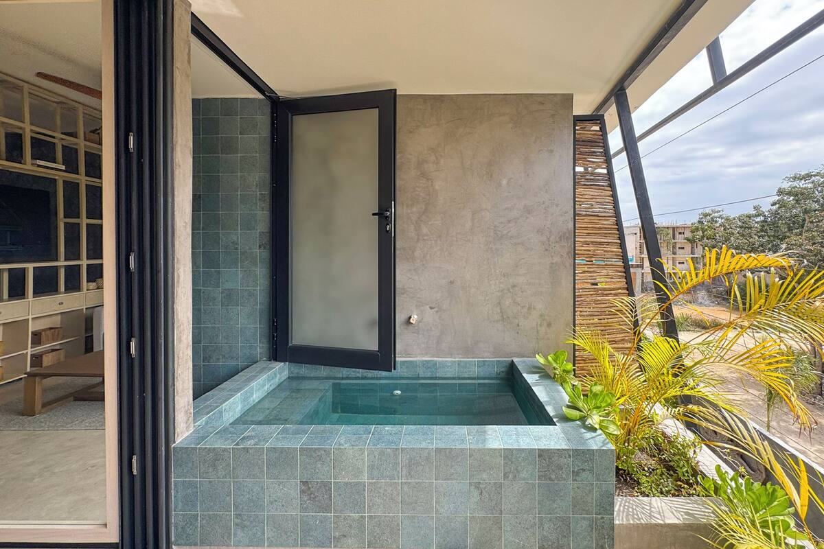 A modern bathroom with a glass door, a built-in bathtub, and a view of the surrounding area.