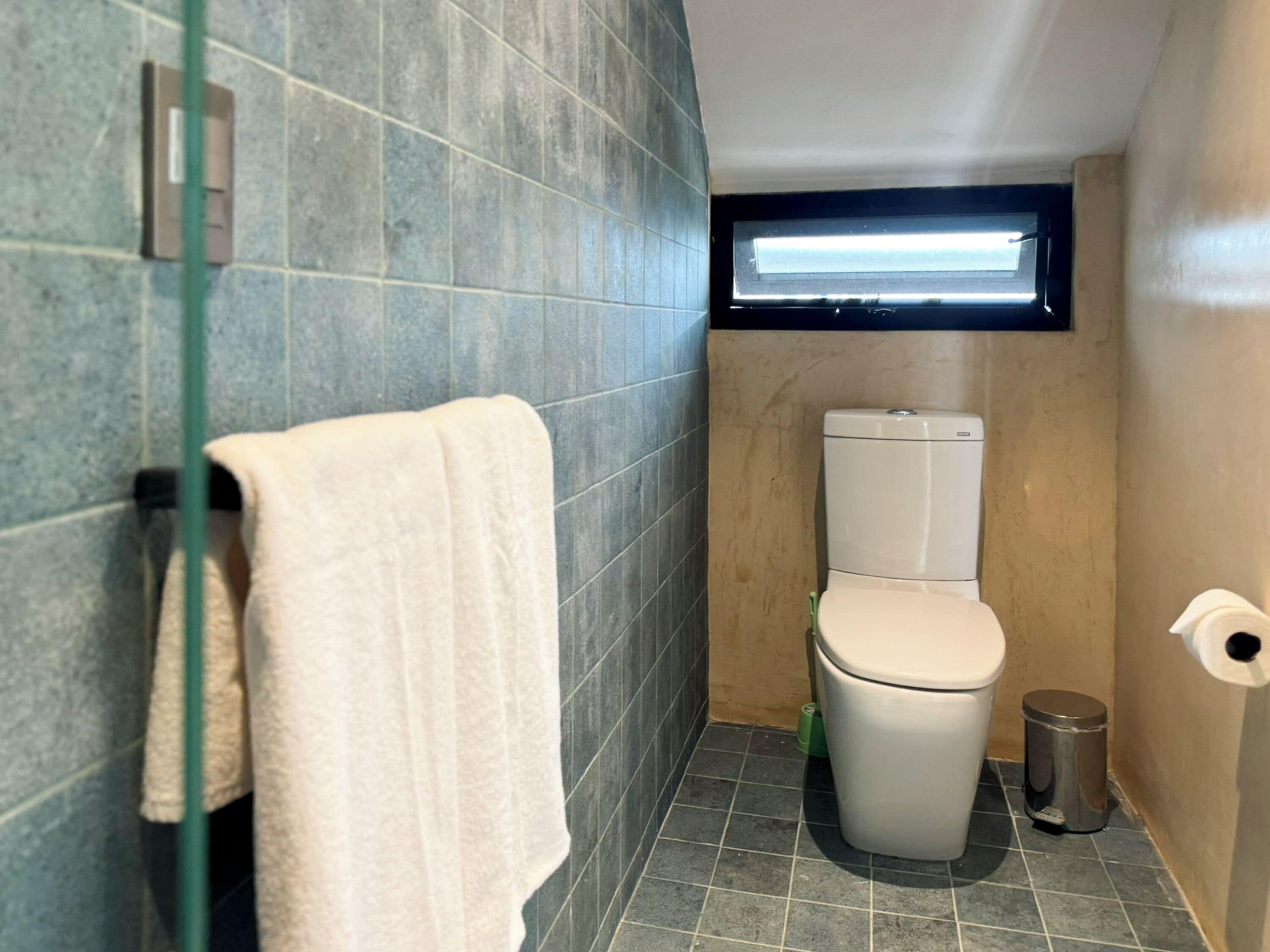 Une petite salle de bain comprenant des toilettes, un porte-serviettes et une poubelle.