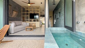 A modern living room with a sofa, coffee table, and TV, leading to a bathroom with a shower and tiled walls. - Zel-va Tulum (Tulum)