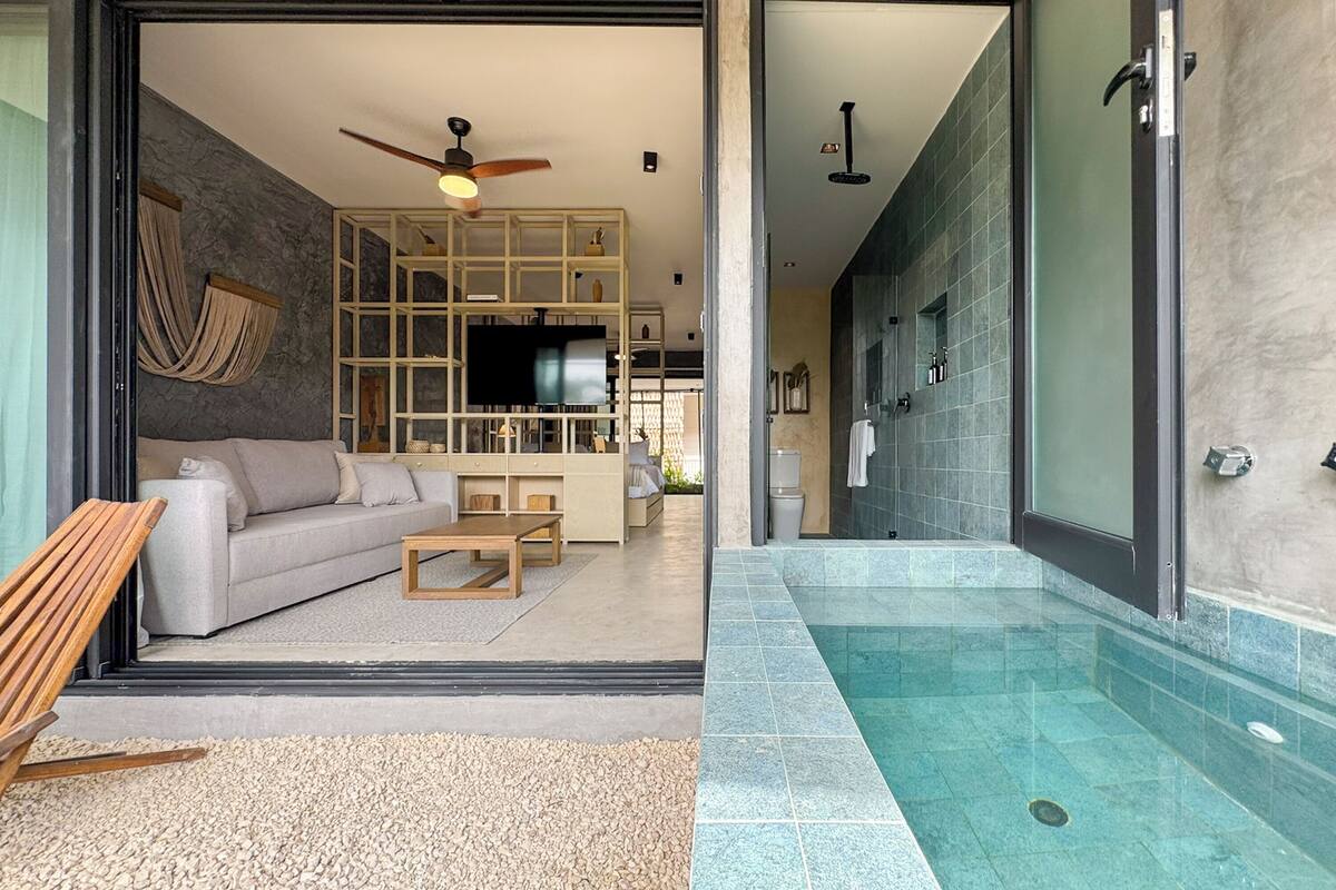A modern living room with a sofa, coffee table, and TV, leading to a bathroom with a shower and tiled walls.
