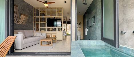 Un salon moderne comprenant un canapé, une table basse et un téléviseur, donnant sur une salle de bain avec une douche et des murs carrelés.