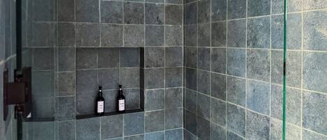 A shower area with a glass door, a showerhead, and two bottles of shampoo on a shelf.