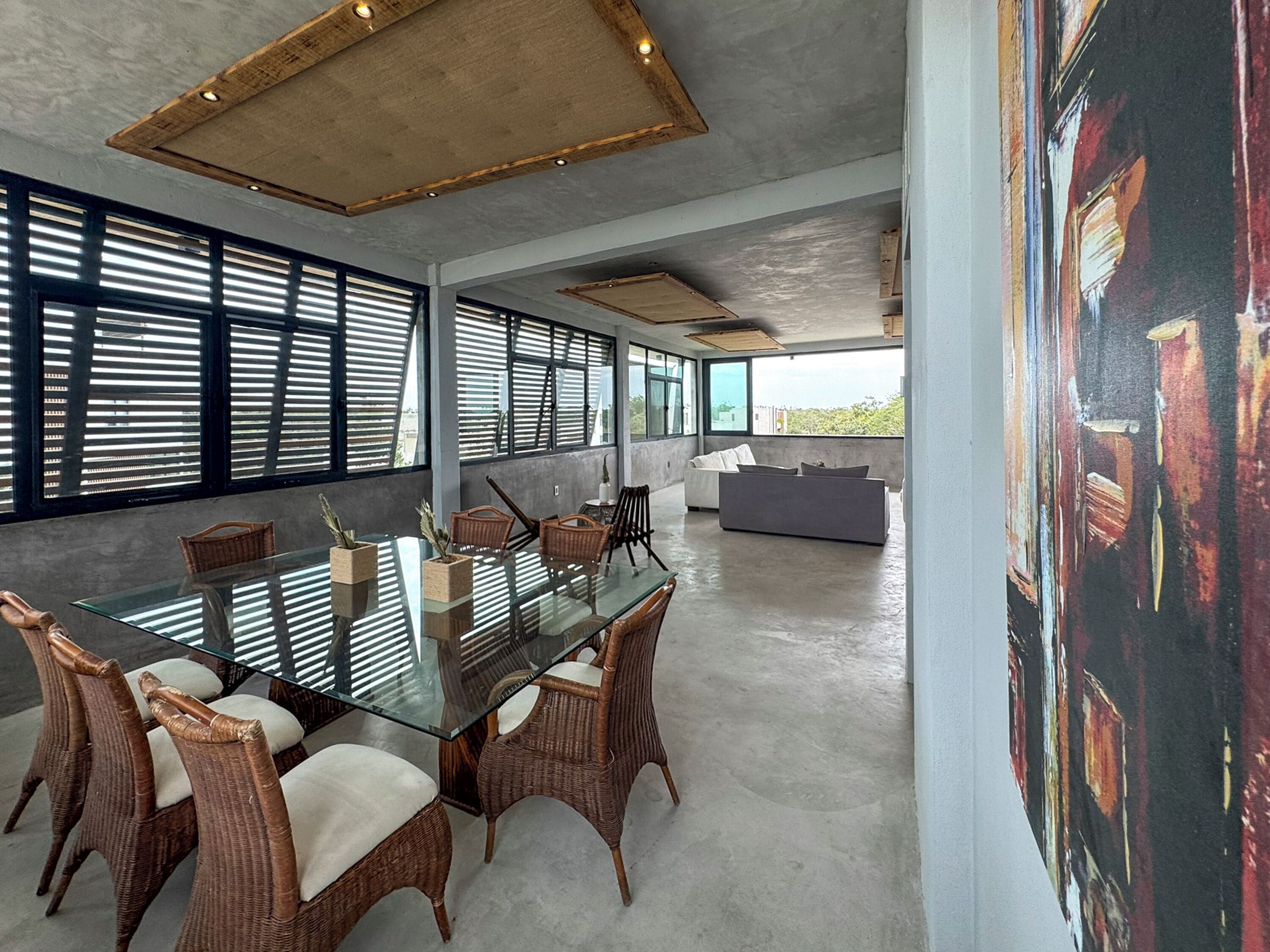 A modern dining area with a glass table, wicker chairs, and a view of the city through large windows.