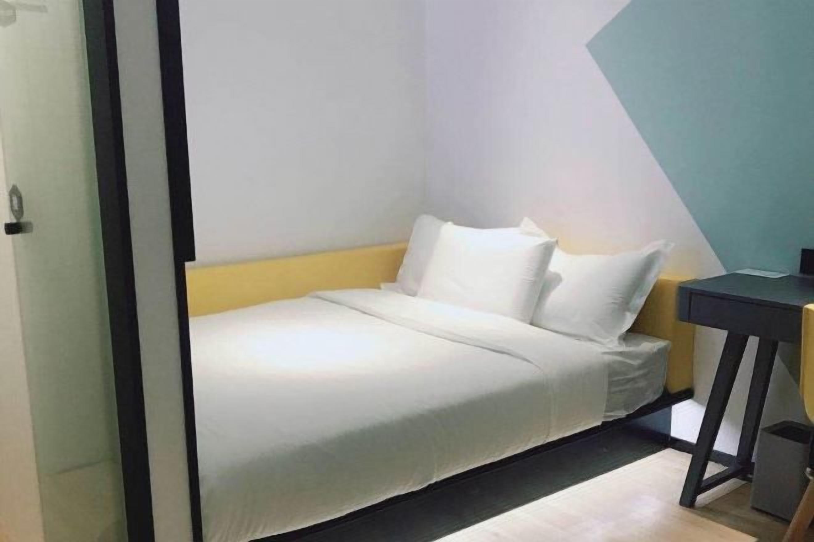 Quarto pequeno e moderno com uma cama, uma mesinha de cabeceira e uma escrivaninha.