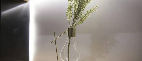Eine birnenförmige Vase mit einer Pflanze auf einem Holzregal vor einer schlichten Wand.