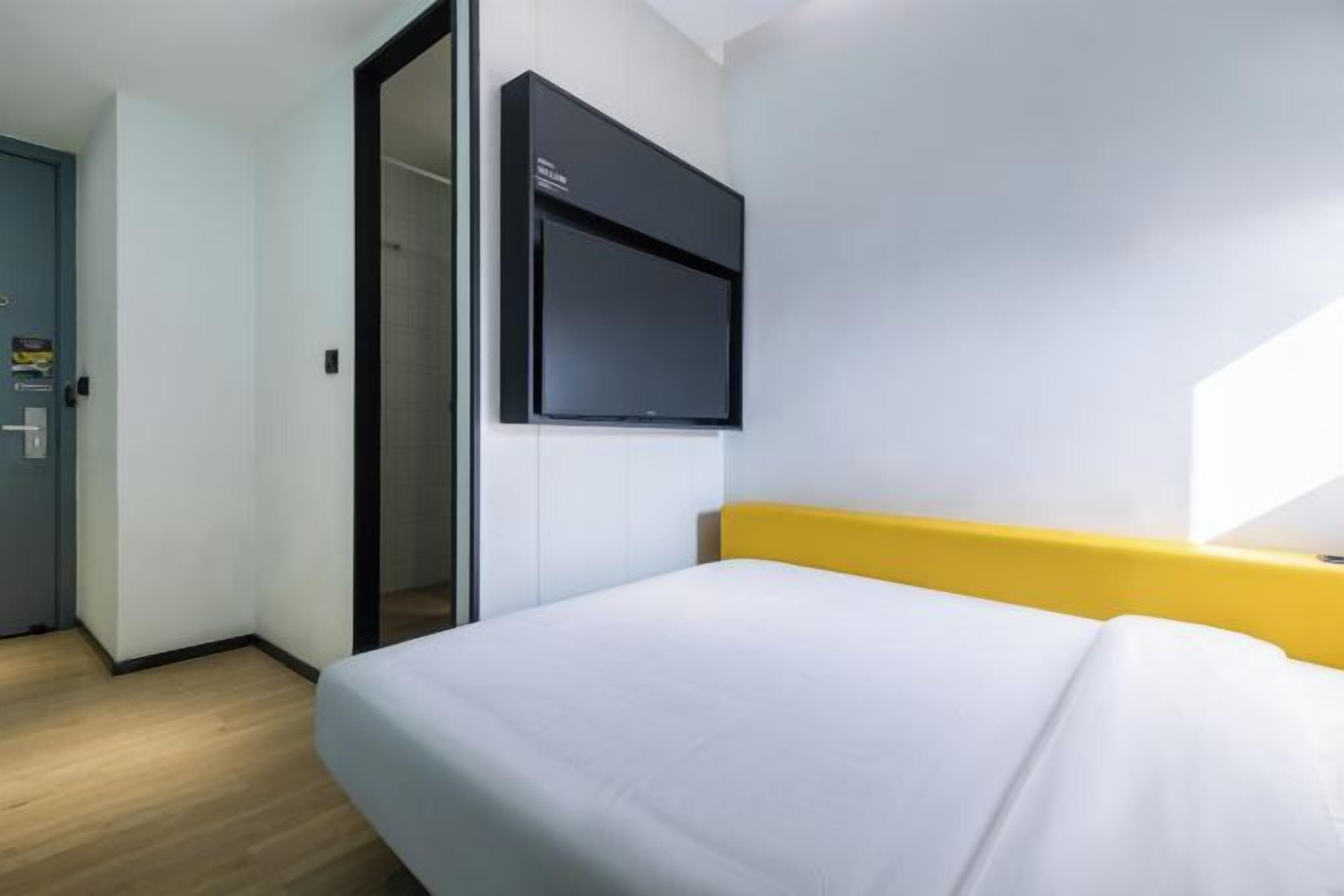 Quarto de hotel com cama, televisão fixada na parede e porta de acesso a outro aposento.