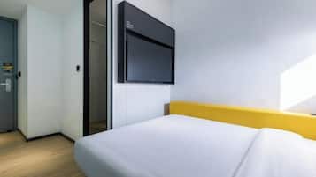 Quarto de hotel com cama, televisão fixada na parede e porta de acesso a outro aposento.
