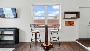 A room with a round wooden table and two chairs, a television mounted on the wall, and a door with a 'Welcome' sign.