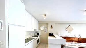 Una cocina compacta con armarios blancos, microondas, lavabo y comedor con mesa y sillas.