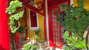 A courtyard with a wooden ceiling, red and yellow walls, and potted plants. - Casa Artística Pousada Leão (Maceio)
