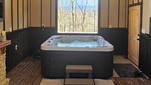 A hot tub in a room with wooden walls and a window overlooking a landscape. - Romantic Mountain view Cabin with Indoor/Outdoor Spa House + Sauna (Ellijay)