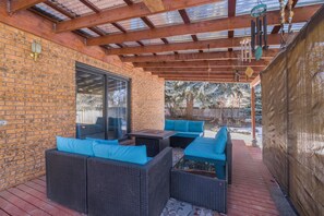 Un patio exterior con mobiliario de mimbre y una puerta de vidrio que da a un área techada.