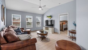 A spacious living room with a brown leather sofa, a glass coffee table, and a flat-screen TV on a white cabinet. - Seaside Canal Retreat: Renovated Home with Private Dock Near Port Aransas (Corpus Christi)