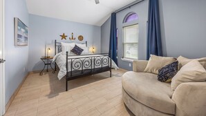 A bedroom with a bed, a ceiling fan, a window with curtains, a bedside table with a lamp, and a sofa. - Seaside Canal Retreat: Renovated Home with Private Dock Near Port Aransas (Corpus Christi)