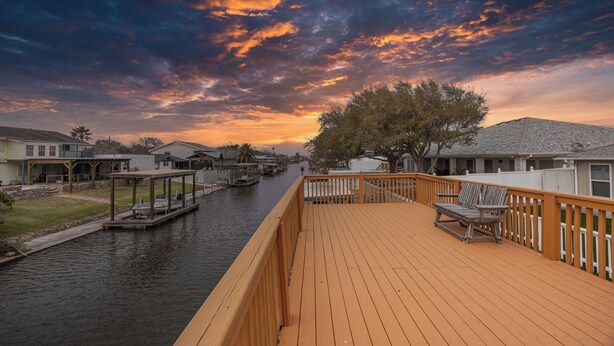 A wooden deck overlooking a canal with houses on one side and a tree on the other. - Seaside Canal Retreat: Renovated Home with Private Dock Near Port Aransas (Corpus Christi)