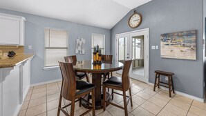 A dining area with a round table, wooden chairs, a chandelier, and a painting on the wall. - Seaside Canal Retreat: Renovated Home with Private Dock Near Port Aransas (Corpus Christi)