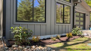A modern house with large windows, a garage, and a landscaped garden with rocks and plants.