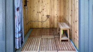 A wooden sauna with a bench, a shower head, and a curtain.
