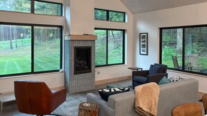 A modern living room with a fireplace, large windows, and a view of a green landscape.