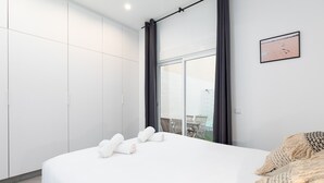 Une chambre d’hôtel moderne avec un grand lit, du linge de lit blanc, une vue sur l’extérieur par une fenêtre et un tableau encadré au mur.