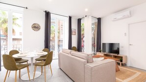 Un salon moderne avec un canapé, une table à manger et des chaises. On y trouve également un téléviseur et une horloge au mur.