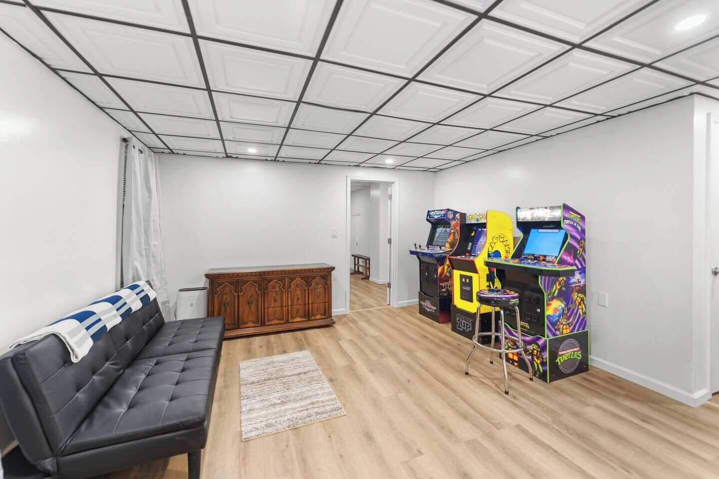 Ein Zimmer mit einer schwarzen Ledersofa, einem Holzschrank und zwei Spielautomaten.