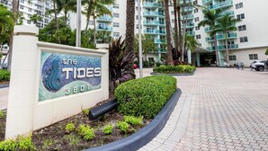 A hotel entrance with a sign reading "The Tides 8801", palm trees, and a flag. - Ocean View Condo, Direct Beach Access, Beach Gear & Cleaning Included (Hollywood)