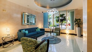 A modern lobby with a blue sofa, patterned armchair, and a glass coffee table. - Ocean View Condo, Direct Beach Access, Beach Gear & Cleaning Included (Hollywood)