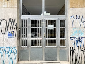 A metal gate with graffiti on the walls, a poster on the left, and a sign above the door.