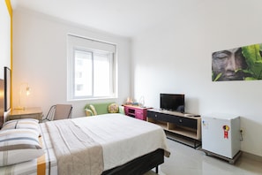 A bedroom with a bed, a desk, a television, and a refrigerator.