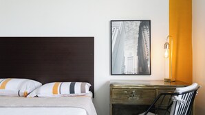 Een hotelkamer met een bed, een bureau, een stoel, een lamp en een lijst met een foto aan de muur.