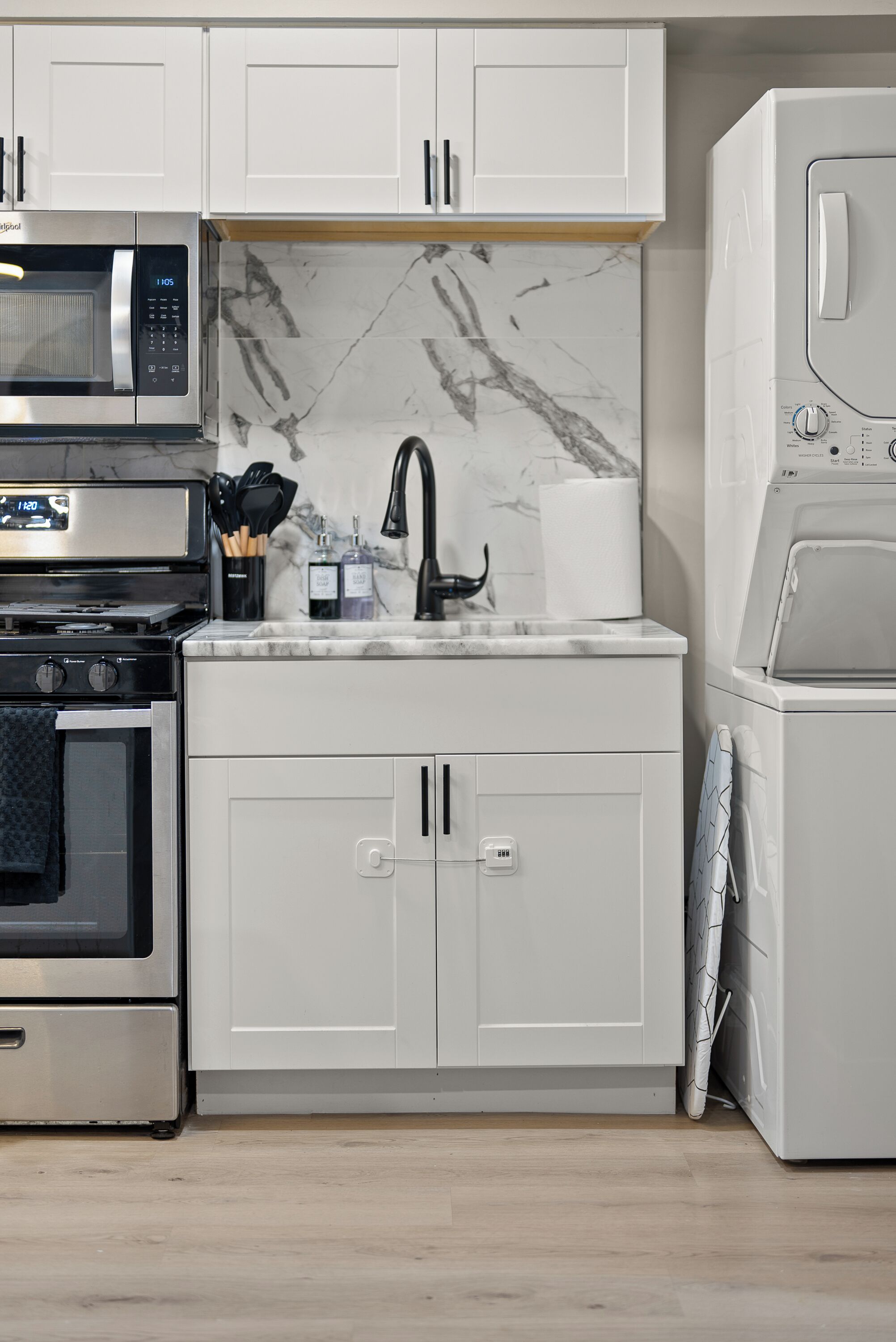 A kitchen with white cabinets, a stainless steel microwave, a built-in oven, a sink with a black faucet, and a built-in washing machine.