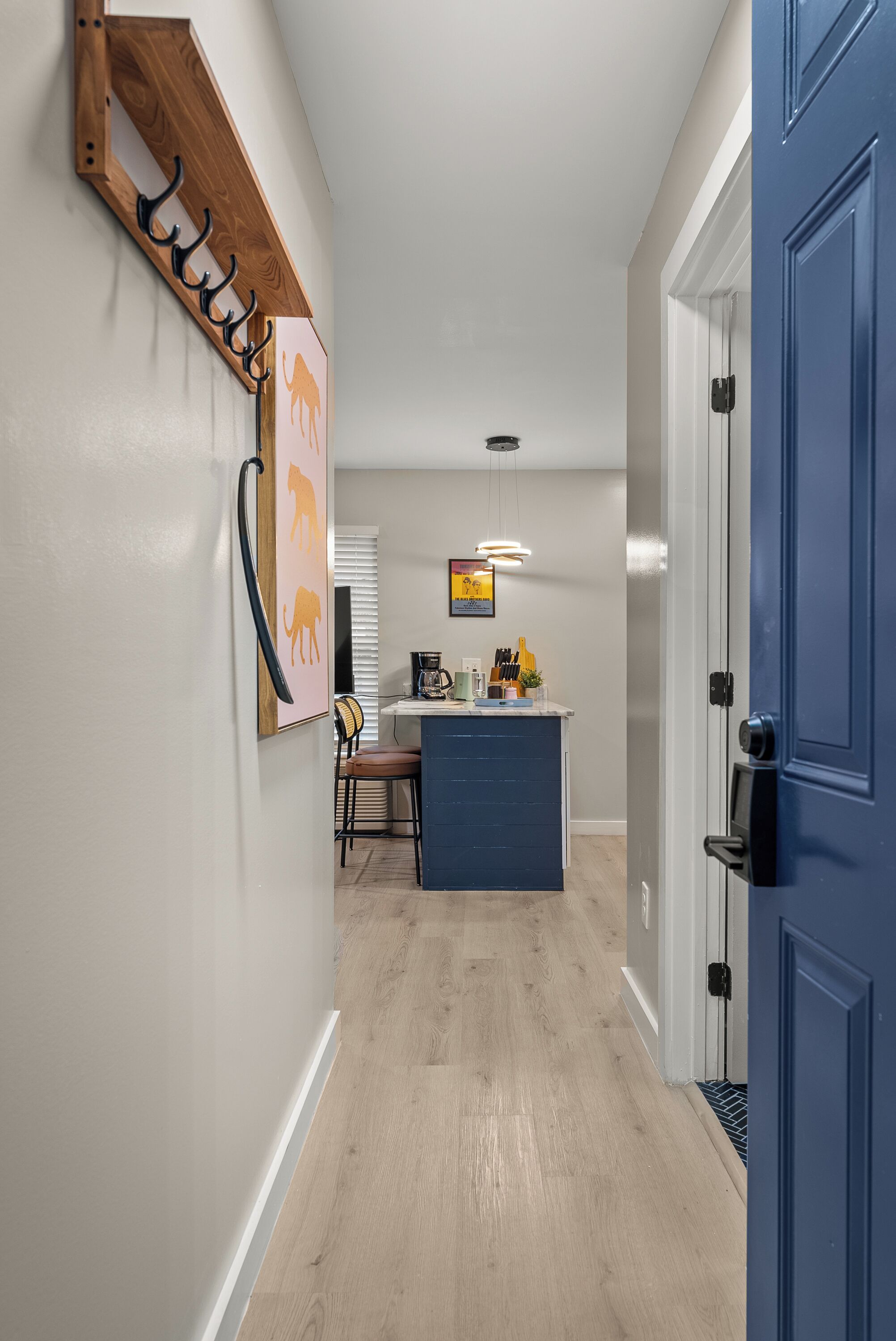 A hallway with a wooden coat rack, a blue door, and a kitchen area with a bar counter.