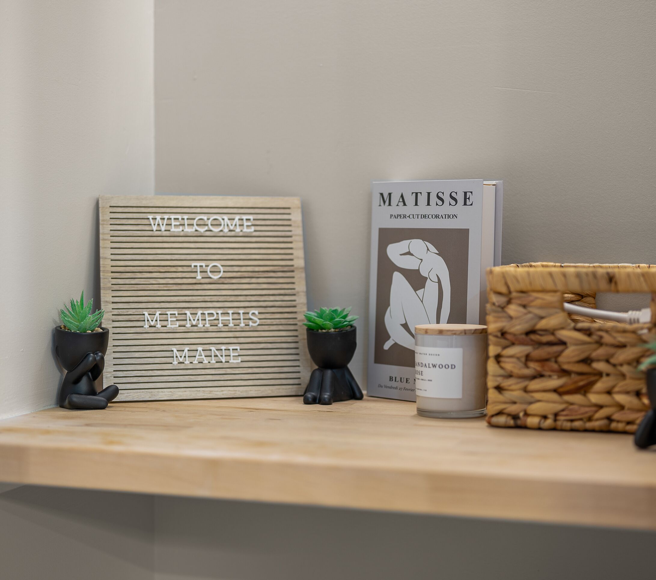 Un letrero de bienvenida, un libro titulado 'Matisse' y una vela sobre una repisa.