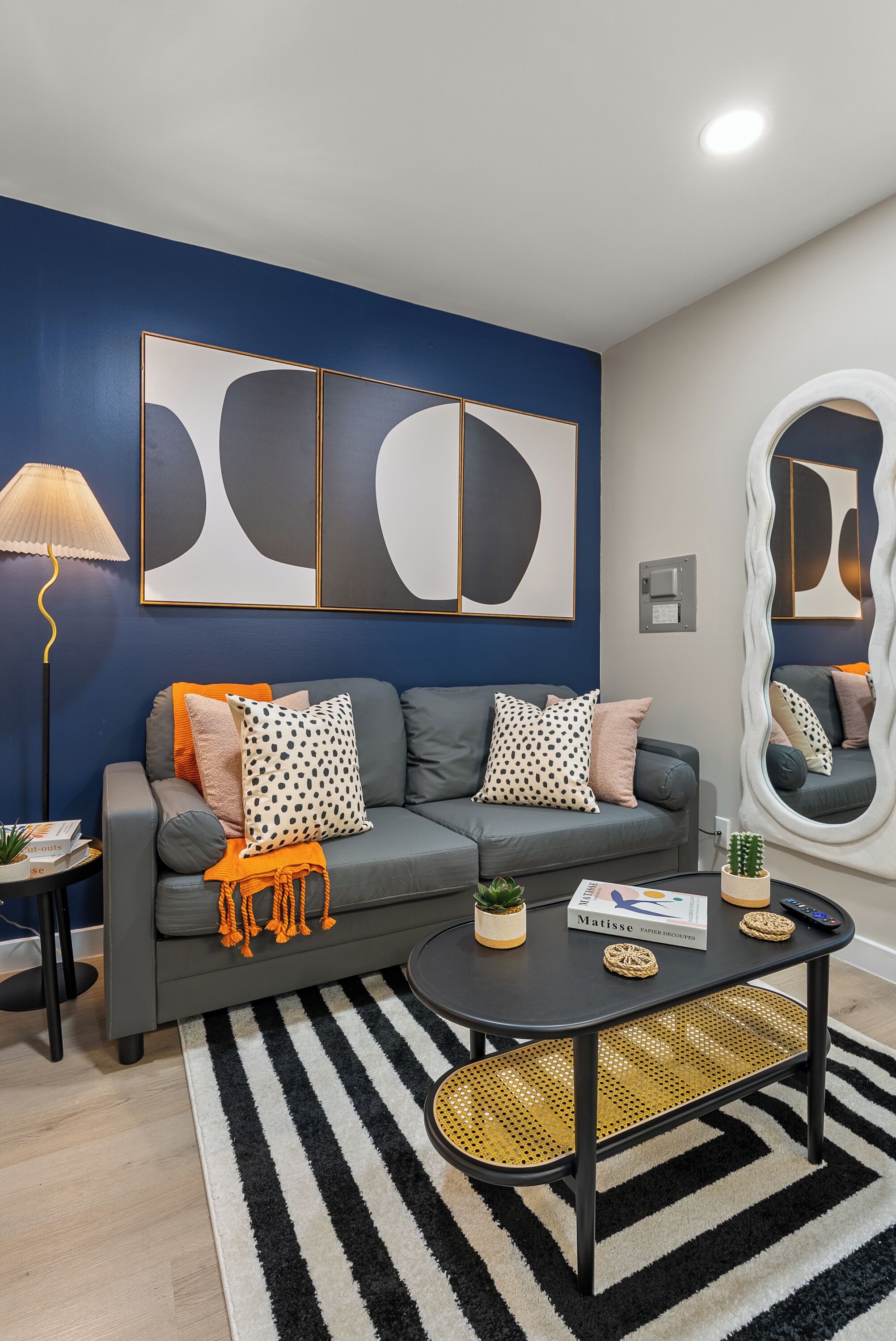 Un salon moderne avec un canapé gris, un tapis rayé noir et blanc et des œuvres d’art abstraites accrochées au mur.