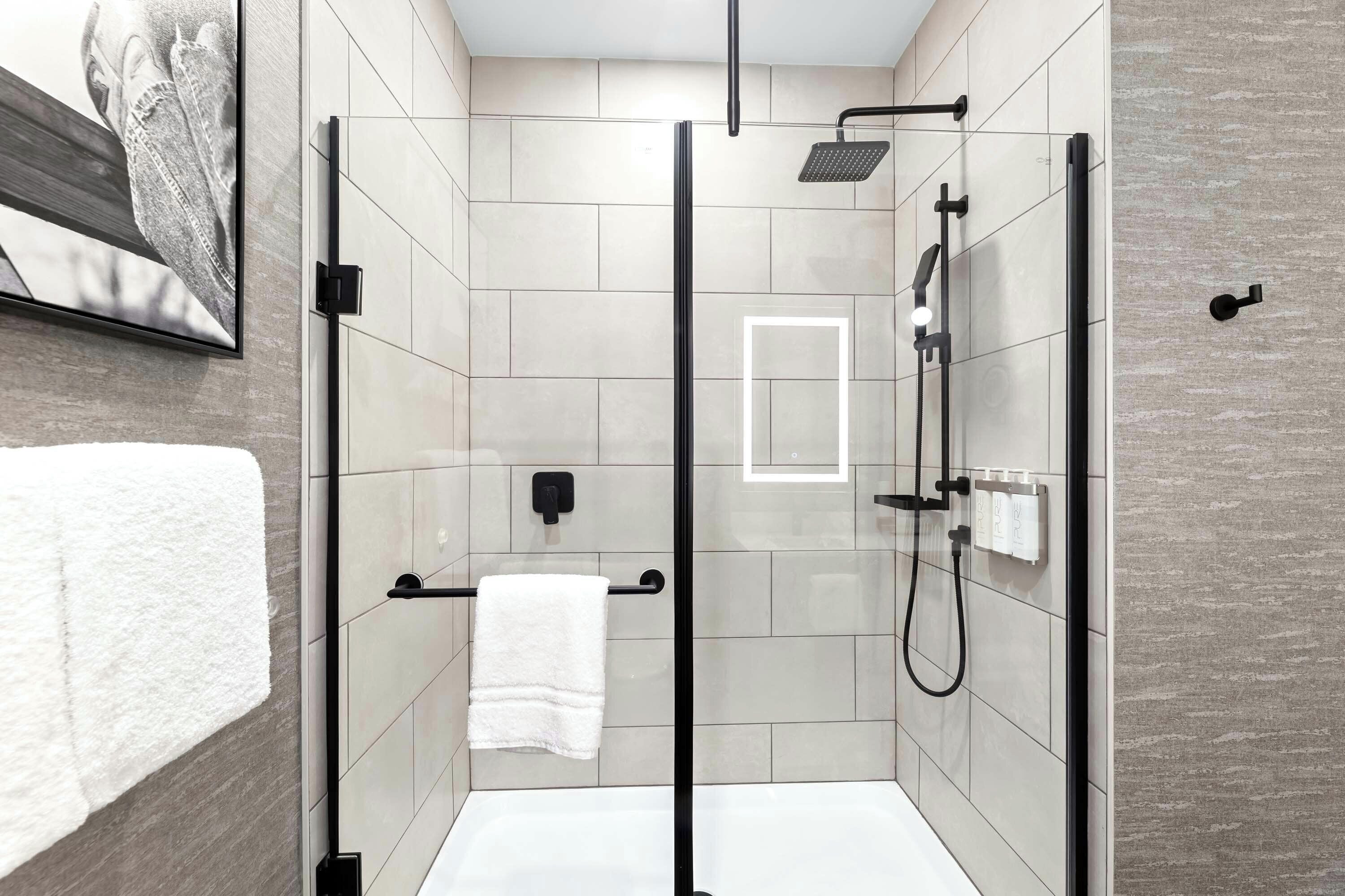 A modern bathroom with a glass-enclosed shower, a white towel on a rack, and a framed picture on the wall.