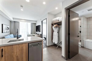 Habitación de hotel moderna con cocina, una mesa de comedor y vestidor con bata colgada.