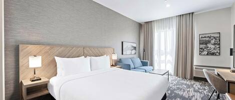 A hotel room with a large bed, a desk, a chair, a nightstand, and a wall-mounted TV.