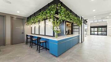 A modern bar area with a blue counter, two bar stools, and hanging plants.