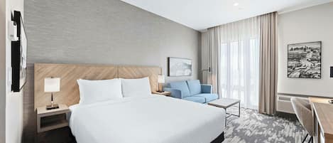 A hotel room with a large bed, a desk, a chair, and a view of the city.