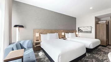 A hotel room with two beds, a sofa, a desk, and a large window.