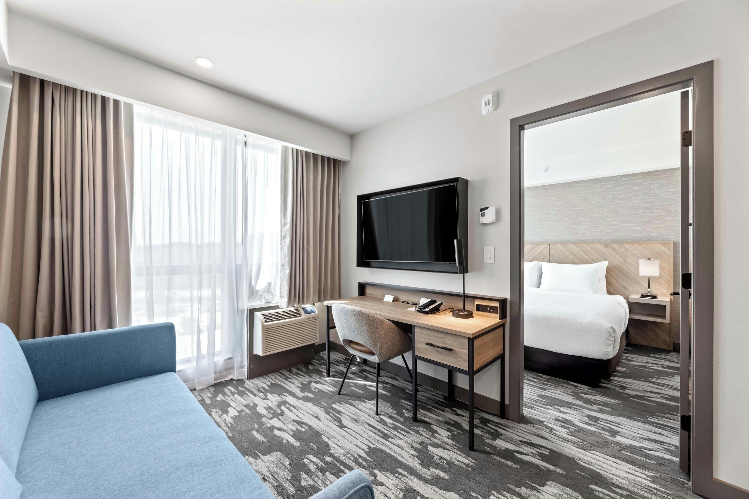 Ein Hotelzimmer mit Bett, Schreibtisch mit Fernseher, Stuhl und großem Spiegel.