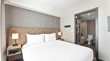 A hotel room with a large bed, bedside tables with lamps, a wooden headboard, and a bathroom visible through an open door.