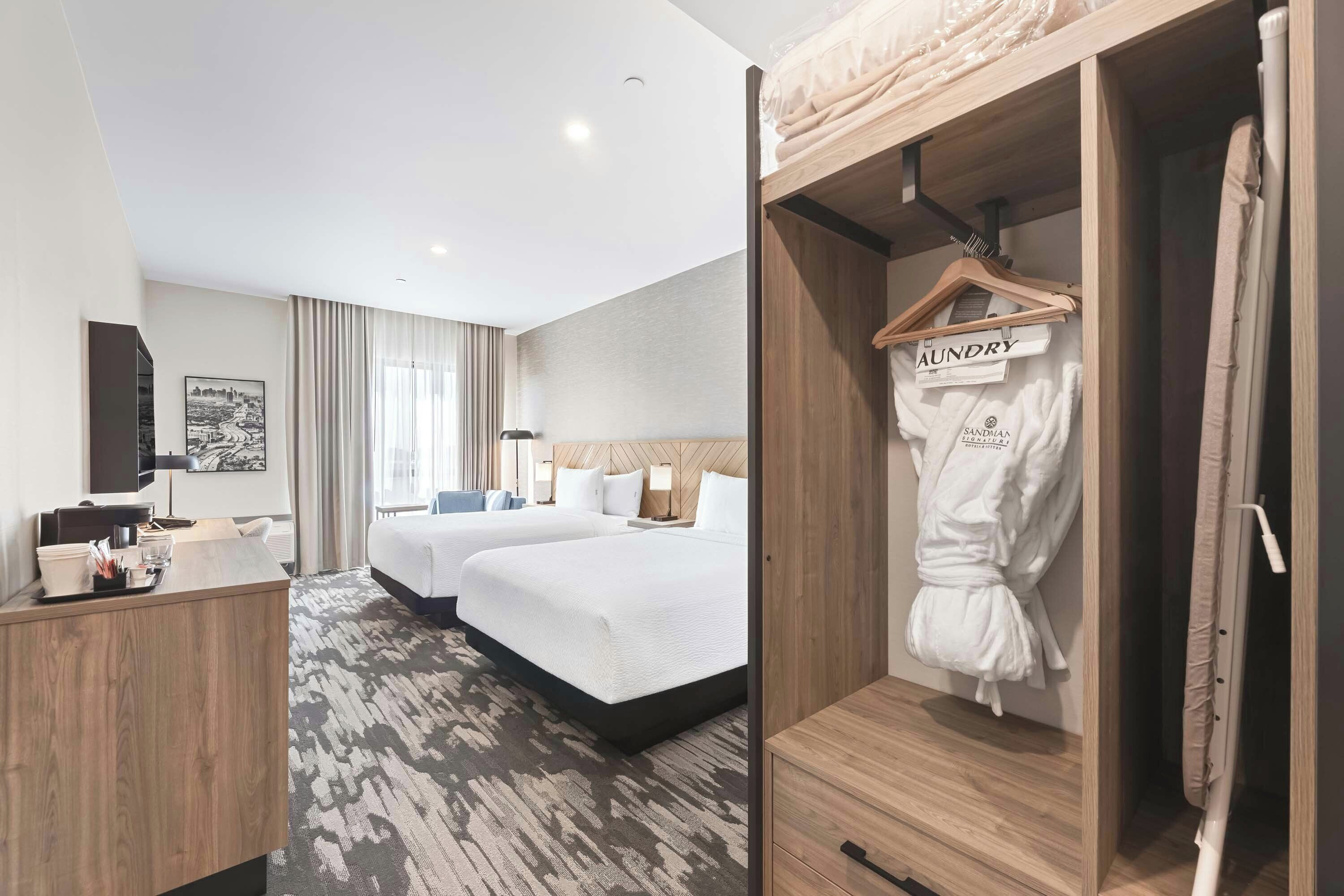 Habitación de hotel con dos camas, un escritorio, un espejo y un armario con bata.