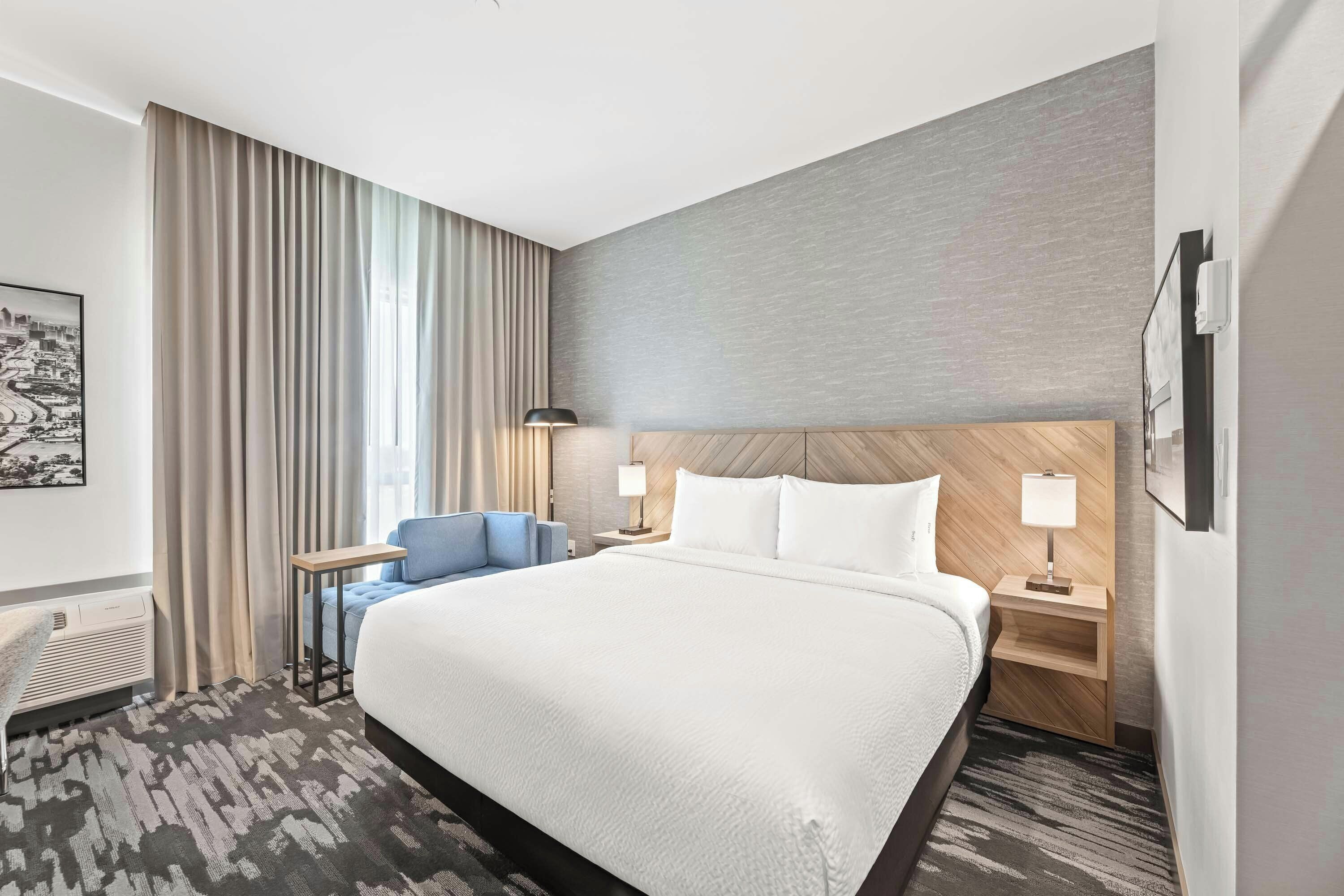Une chambre d’hôtel avec un grand lit, un bureau, une chaise, une table de chevet, une lampe et un climatiseur fixé au mur.