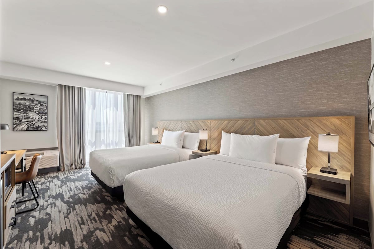 A hotel room with two beds, a desk, and a chair.