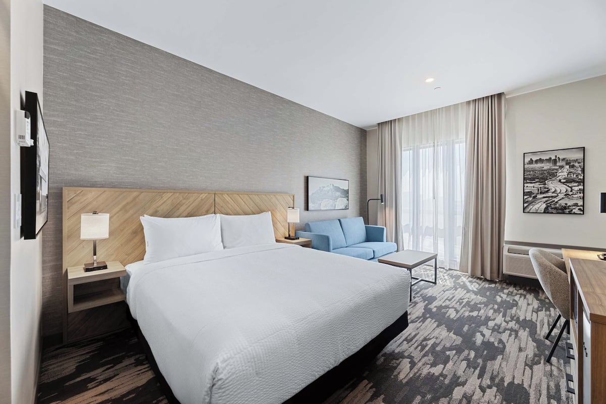 A hotel room with a large bed, a blue sofa, a desk, and a cityscape painting.